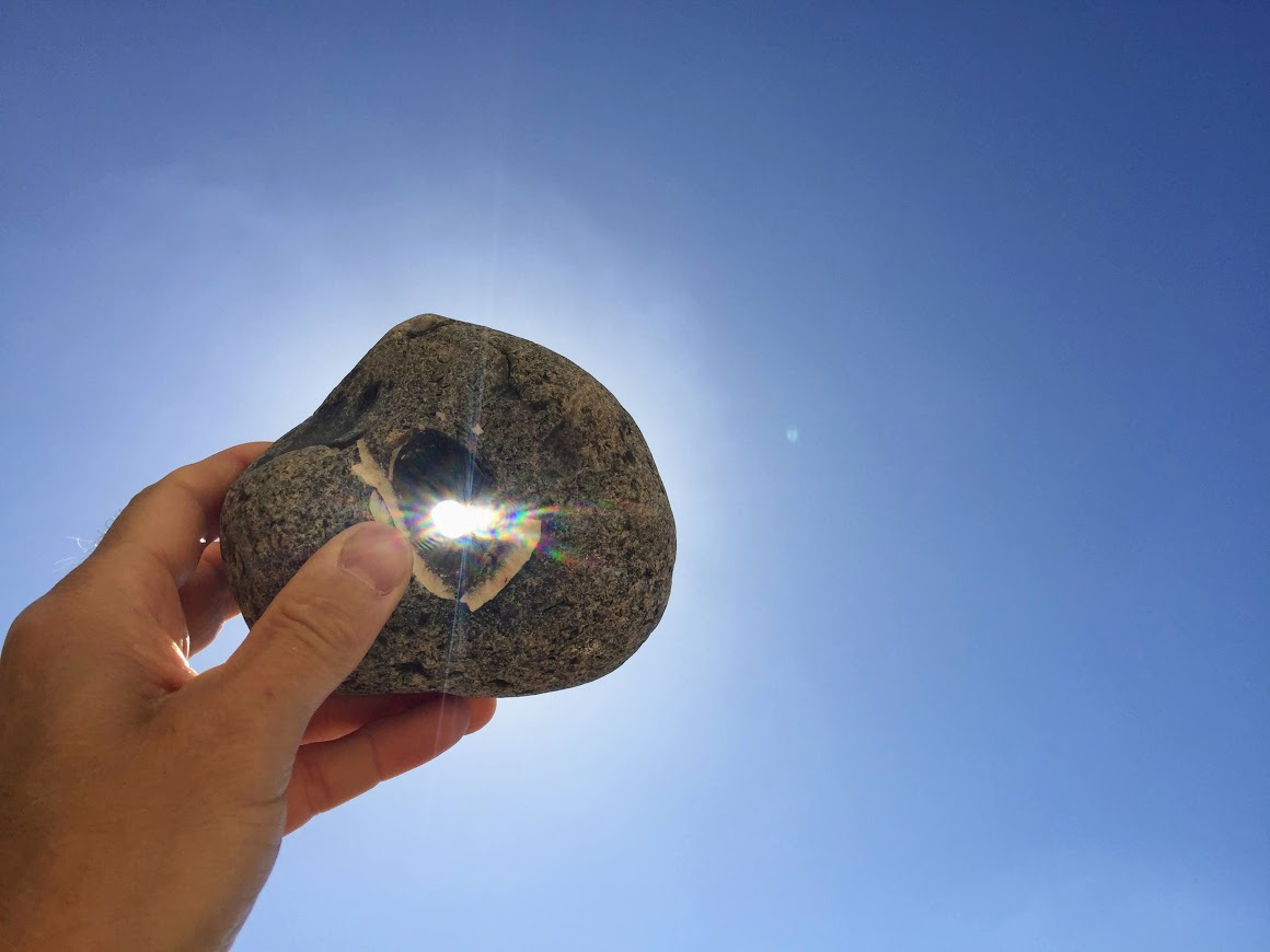 hand holding stone with hole in it against blue sky