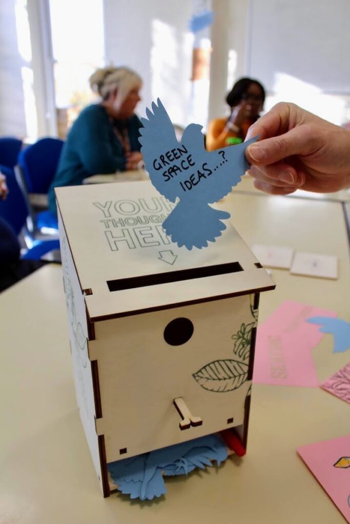 hand holding bird shaped note with 'green space ideas' written on it and bird box