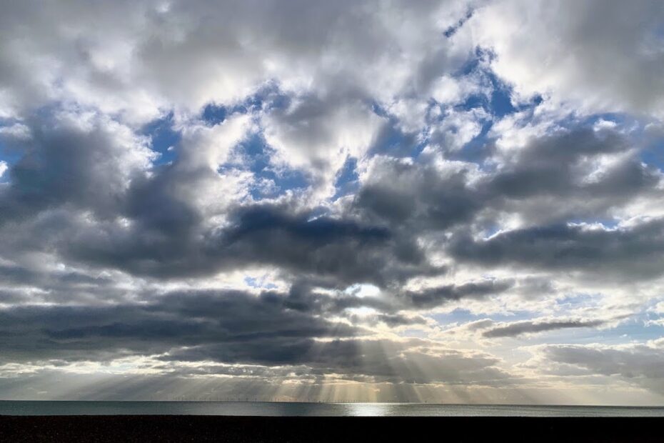sun breaking through clouds over seascape with wind turbines