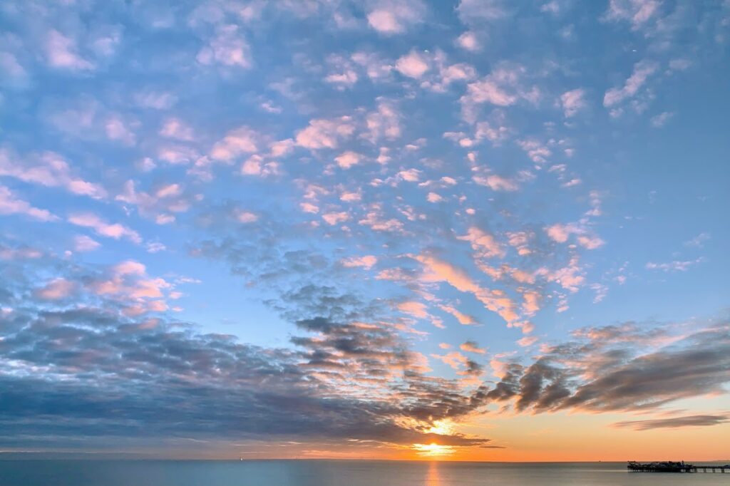 sunset pink clouds over sea with pier