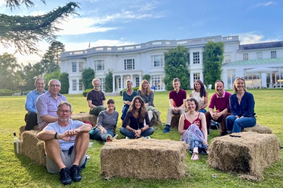 Smiling people sitting on grass and hay bales in sunshine facing camera