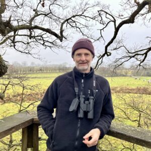 man with beard and hat in treehouse binoculars around neck