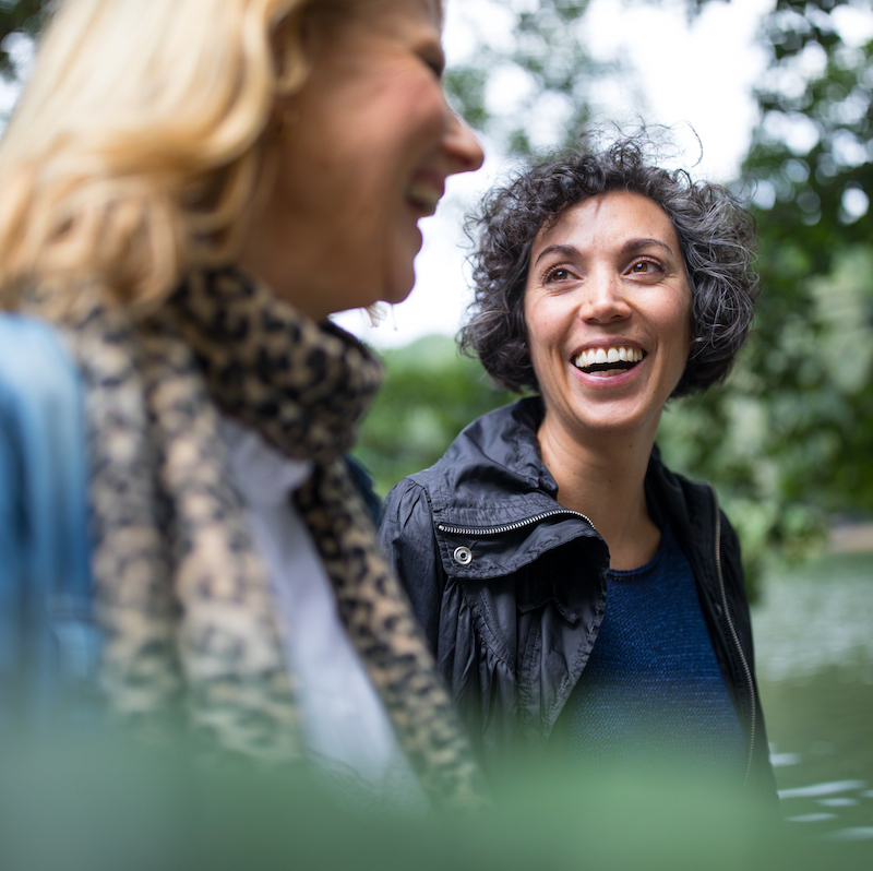 Happy mature woman looking at friend in forest