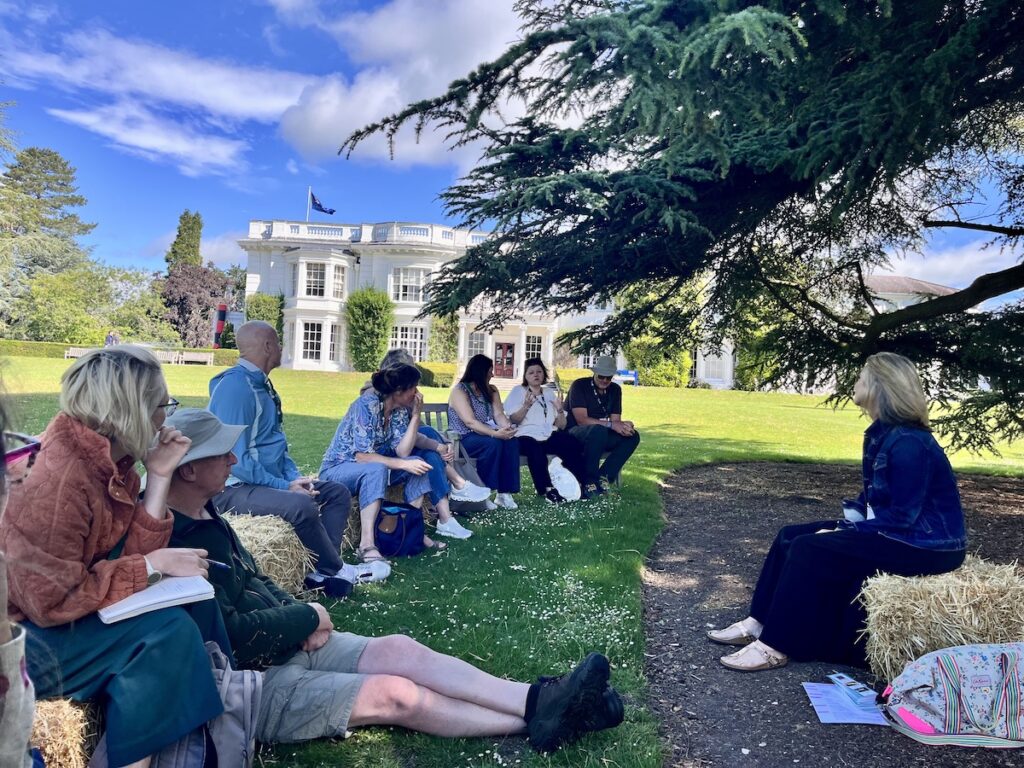 group sitting talking under tree in front of grand house